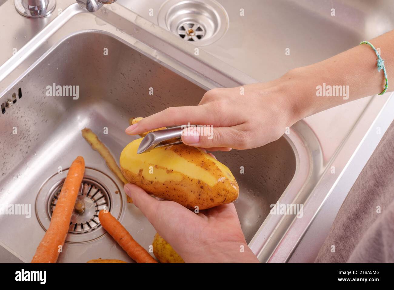 Mains féminines épluchant une pomme de terre dans l'évier dans la cuisine. Légumes, végétariens, préparation pour la cuisine, aliments sains, mode de vie alimentaire Banque D'Images