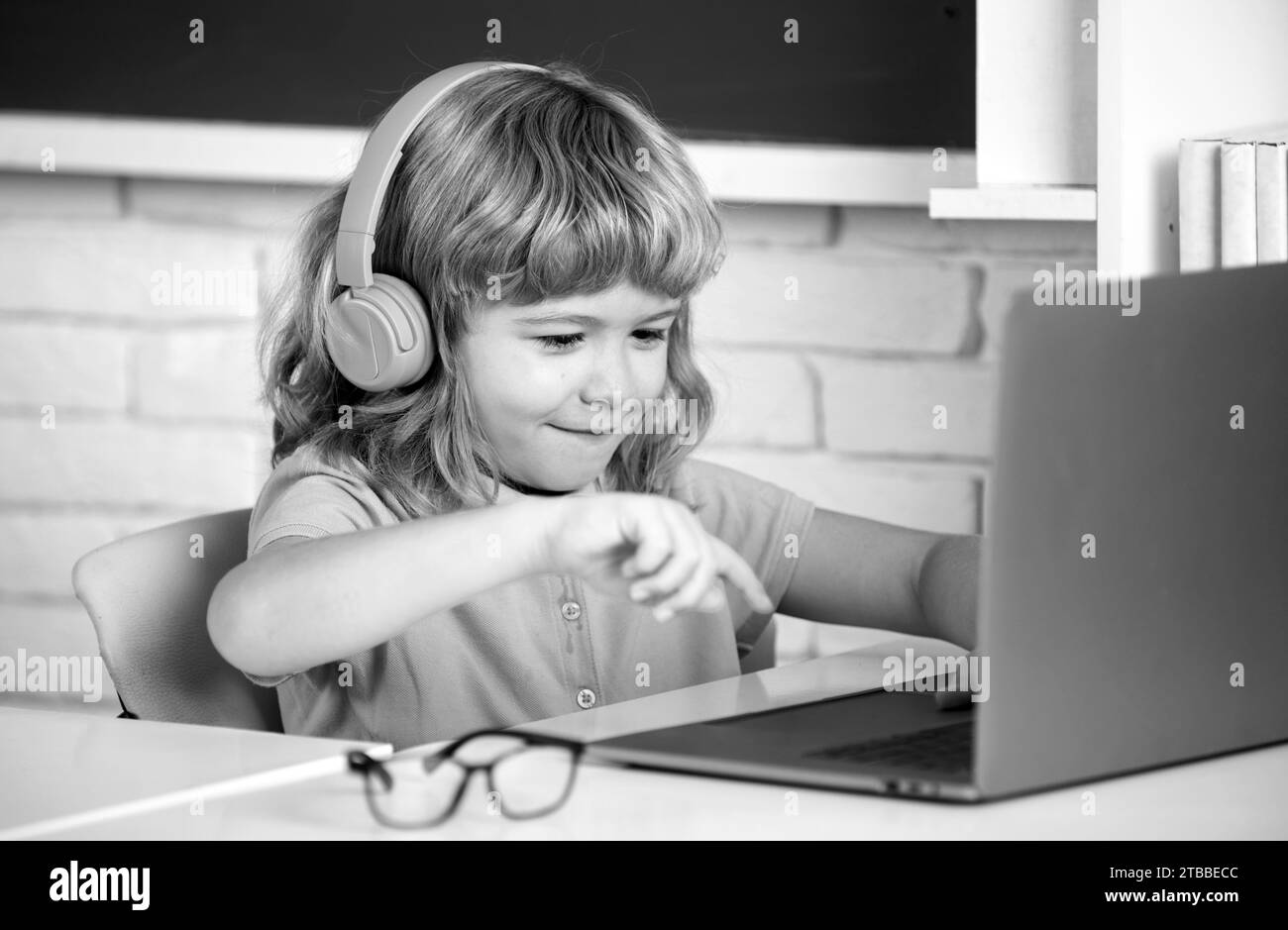 Smart boy dans un casque asseyez-vous au bureau, étudiez en ligne sur un ordinateur portable à l'école, klever Kid porter des écouteurs dans l'apprentissage d'ordinateur portable en utilisant des leçons d'Internet. En ligne l Banque D'Images