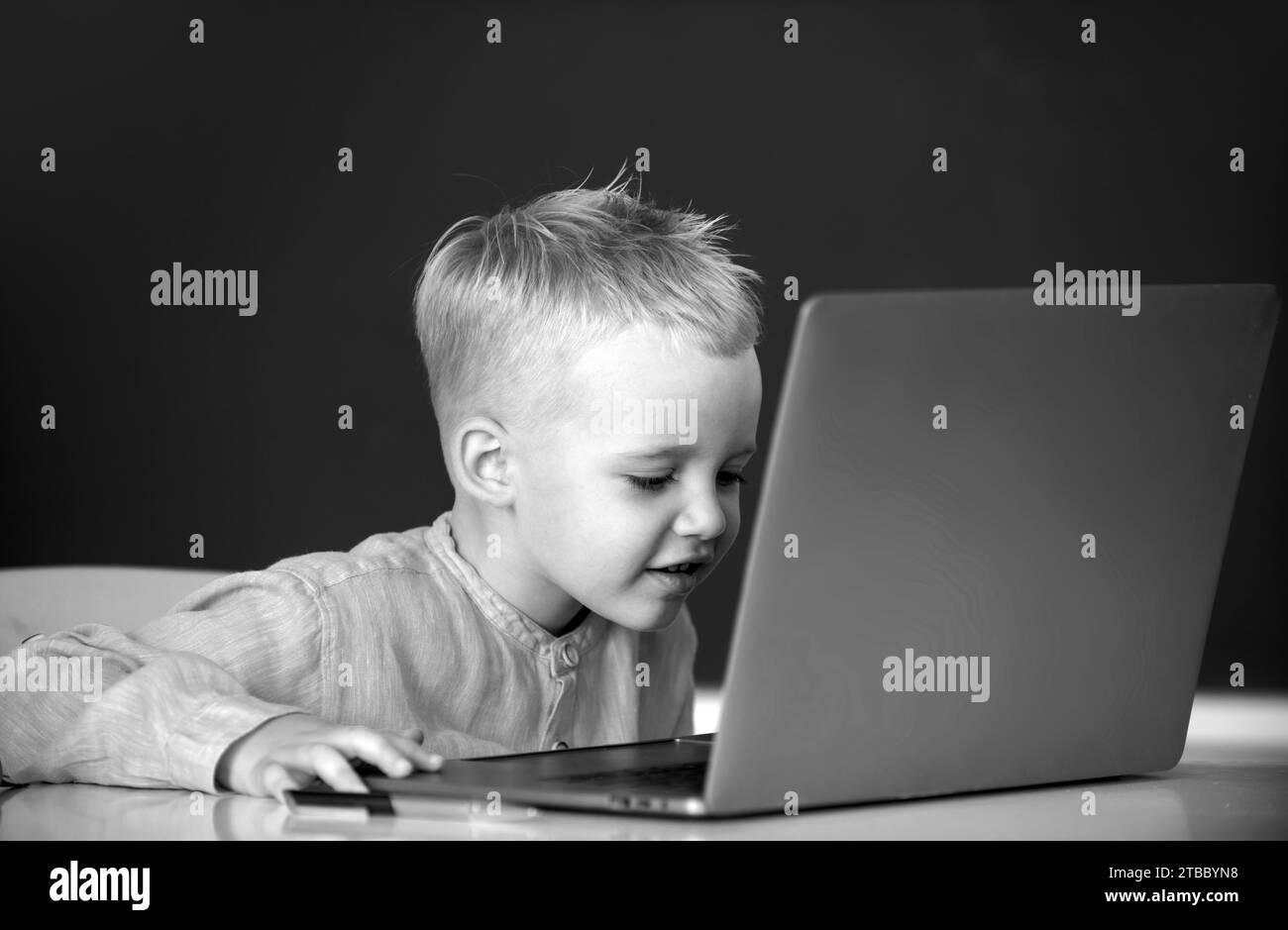 Petit garçon étudiant utilisant un ordinateur portable dans la classe d'école. Pupille blonde drôle au tableau noir Banque D'Images