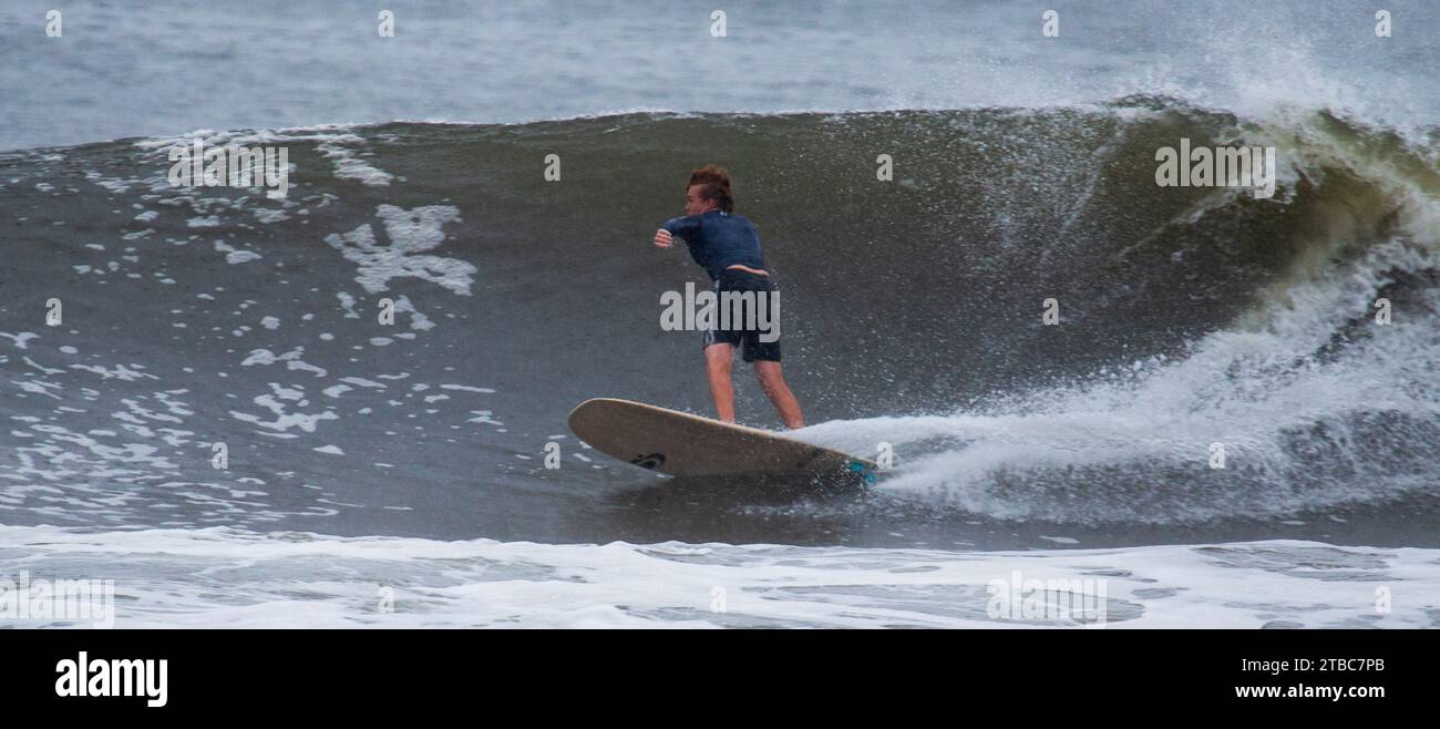 Gilgo Beach, New York, États-Unis - 31 août 2023 : un homme chevauchant une grande vague sur une planche de surf sous la pluie. Banque D'Images