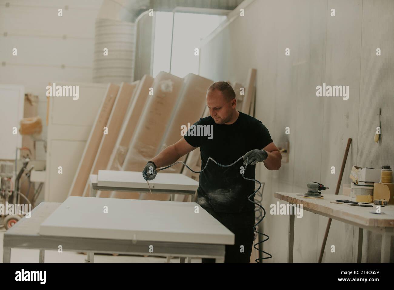 Un travailleur dévoué dans l'industrie du bois emploie l'air comprimé pour nettoyer méticuleusement les produits en bois dans leur phase finale, illustrant Banque D'Images