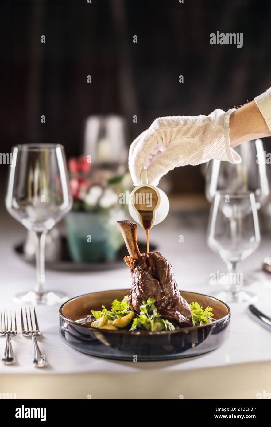 Le chef ou le serveur termine le repas directement sur la table du restaurant, en versant la sauce sur le gigot d'agneau confit. Banque D'Images