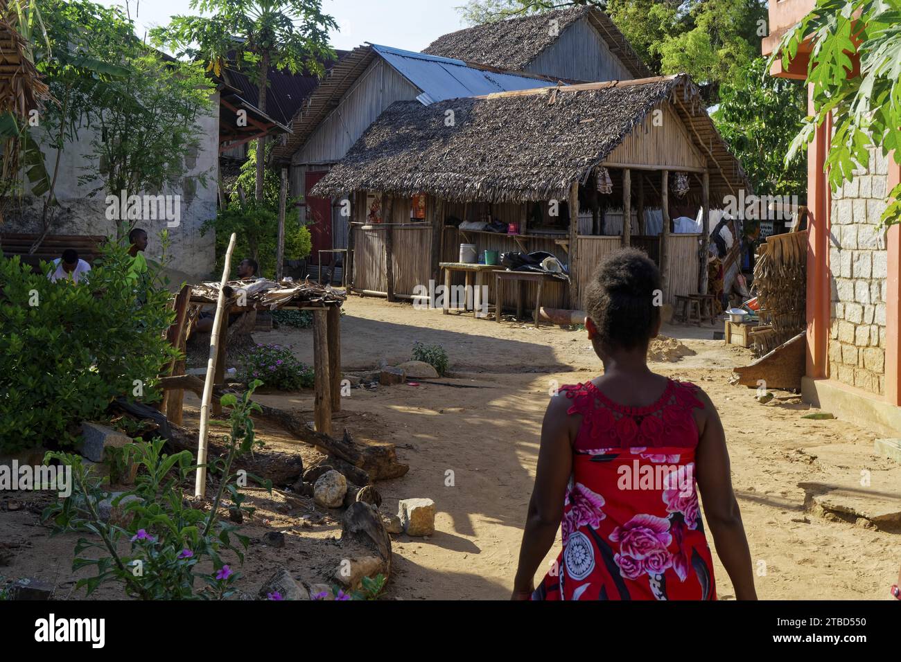 Rue du village, femme en robe rouge, cabane en chaume, Ampangorinana, Nosy Komba, Madagascar Banque D'Images