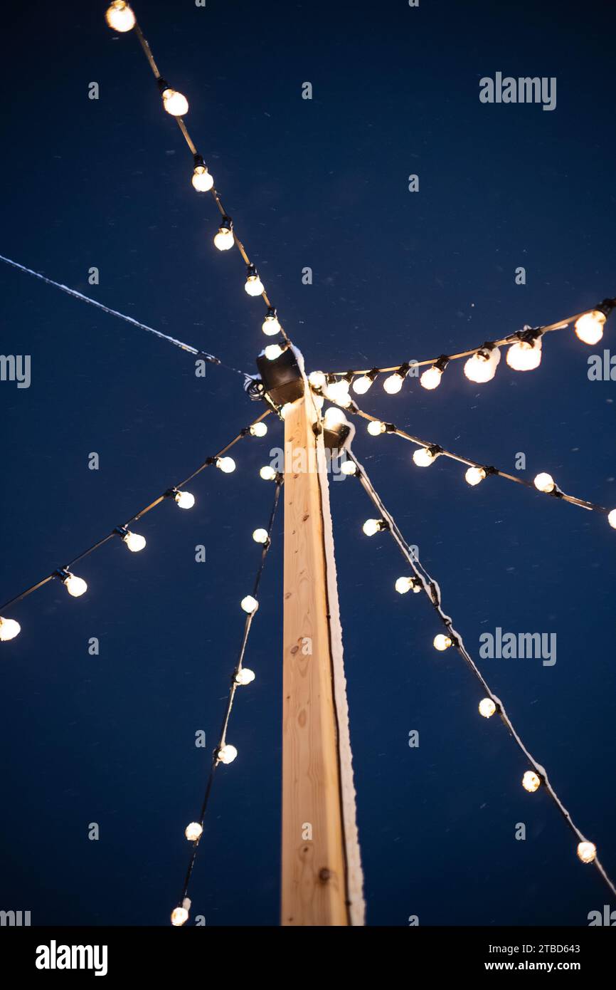 Guirlande lumineuse décorative suspendue à un poteau en bois. Ampoules de tungstène, ciel bleu foncé, vue à faible angle, pas de gens. Banque D'Images