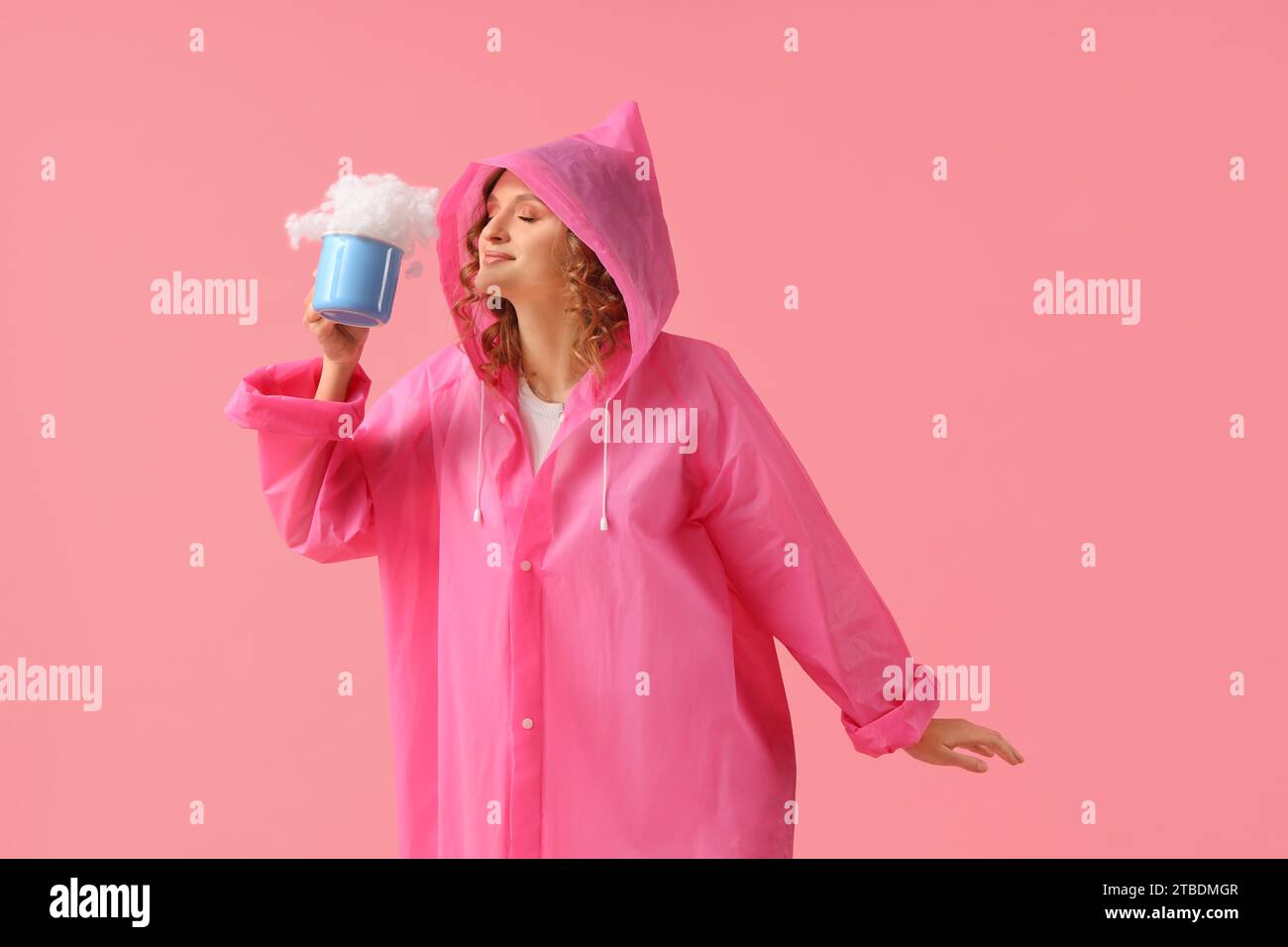 Jeune femme en imperméable avec tasse de nuage sur fond rose Banque D'Images