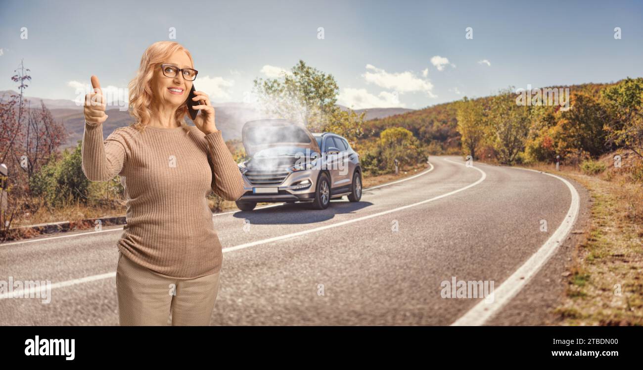Femme avec un problème de voiture appelant une société de service de voiture et faisant des gestes pouces vers le haut sur une route ouverte Banque D'Images