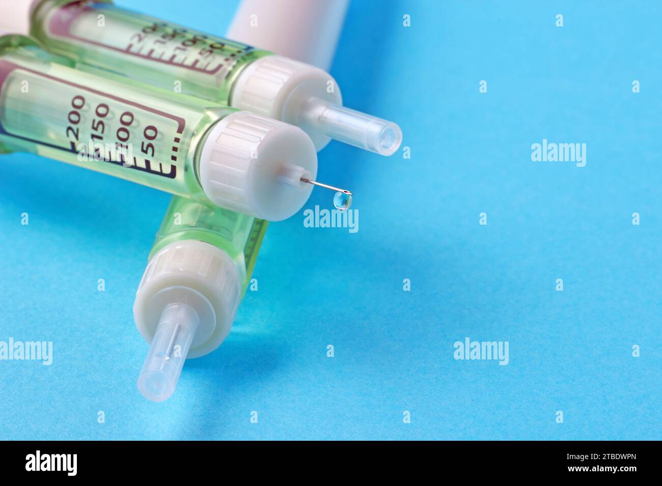 Stylo de seringue d'insuline avec une goutte d'insuline à l'extrémité de l'aiguille sur un fond bleu. Banque D'Images
