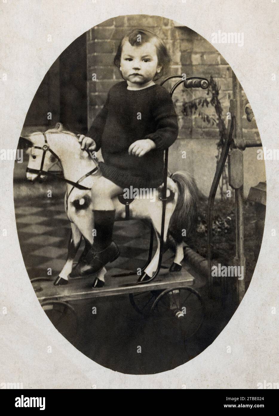 Un enfant sur un cheval jouet à l'extérieur de la maison. Banque D'Images