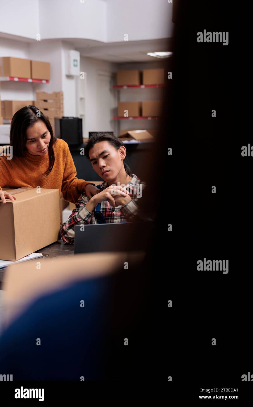 Préparateurs de commandes d'entrepôt équipe asiatique analysant les informations sur les produits sur ordinateur portable. Employés de magasin de service postal gérant l'optimisation d'itinéraire d'expédition de colis sur ordinateur dans la salle de stockage Banque D'Images