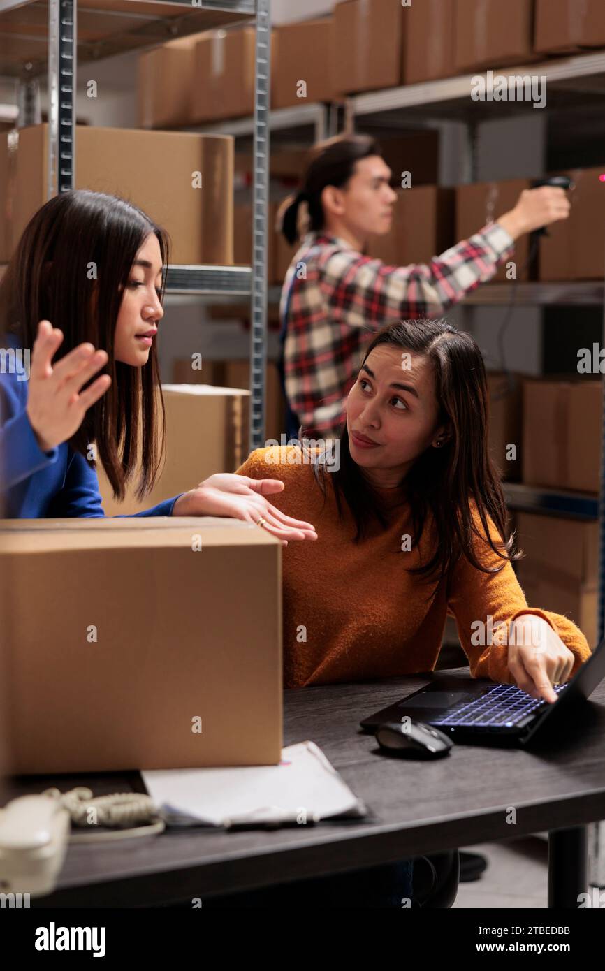 Opérateur d'entrepôt supervisant un collègue faisant l'inventaire sur ordinateur portable dans la salle de stockage. Magasin de jeunes femmes asiatiques employées discutant de la logistique des marchandises et le calendrier de distribution Banque D'Images