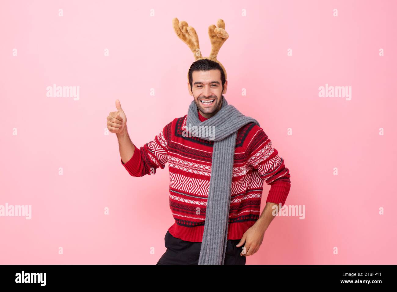 Le studio de Noël a photographié le portrait d'un homme caucasien souriant portant un chandail et un bandeau de renne fantaisie donnant des pouces vers le haut dans un fond isolé de couleur rose Banque D'Images