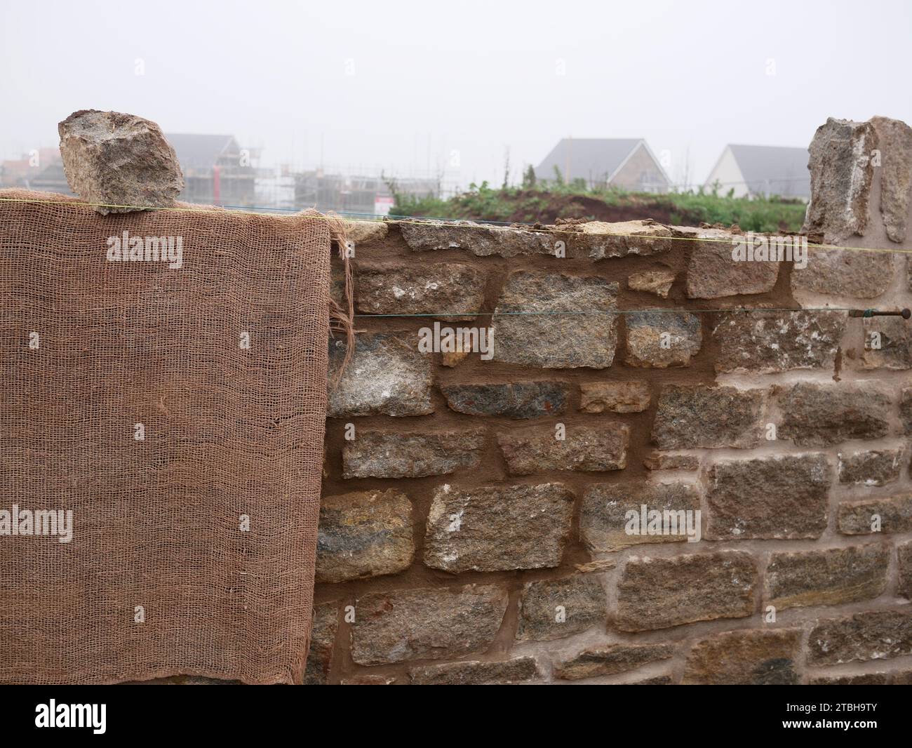 Mur d'enceinte avec façade traditionnelle en pierre en cours de construction dans un nouveau développement immobilier. Hessian protège la nouvelle maçonnerie du froid. Banque D'Images