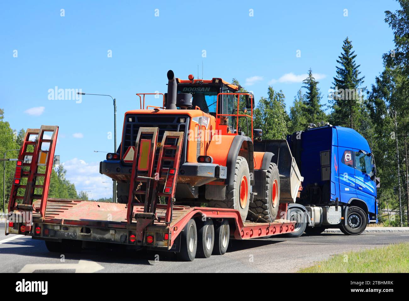 Blue Volvo FH Truck transporte le chargeur sur pneus Doosan DL 450 sur une remorque col de cygne le long de la route, en tournant à droite. Vue arrière. Salo, Finlande. 12 août 2022. Banque D'Images