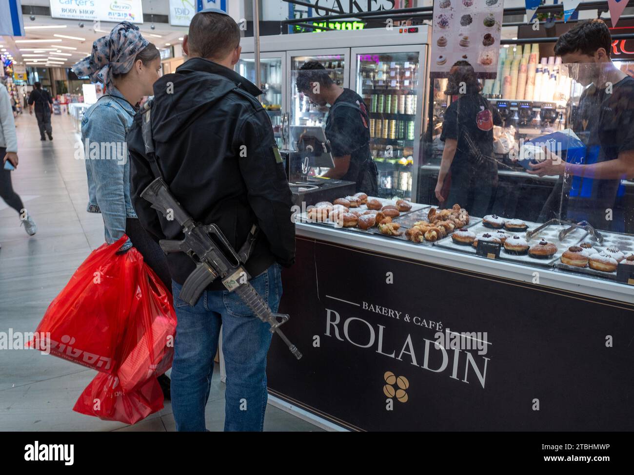 Mevaseret Zion, Israël. 07 décembre 2023. Un couple juif, avec un fusil d’assaut M-16 et un clip chargé, achète des beignets de gelée dans un centre commercial avant le début de Hanoukka à Mevaseret Zion, à l’extérieur de Jérusalem, Israël, le jeudi 7 décembre 2023. La fête juive de Hanukkah qui commence au coucher du soleil ce soir commémore la récupération de Jérusalem et la redédicace ultérieure du second Temple au 2e siècle avant notre ère. Photo de Jim Hollander/UPI crédit : UPI/Alamy Live News Banque D'Images