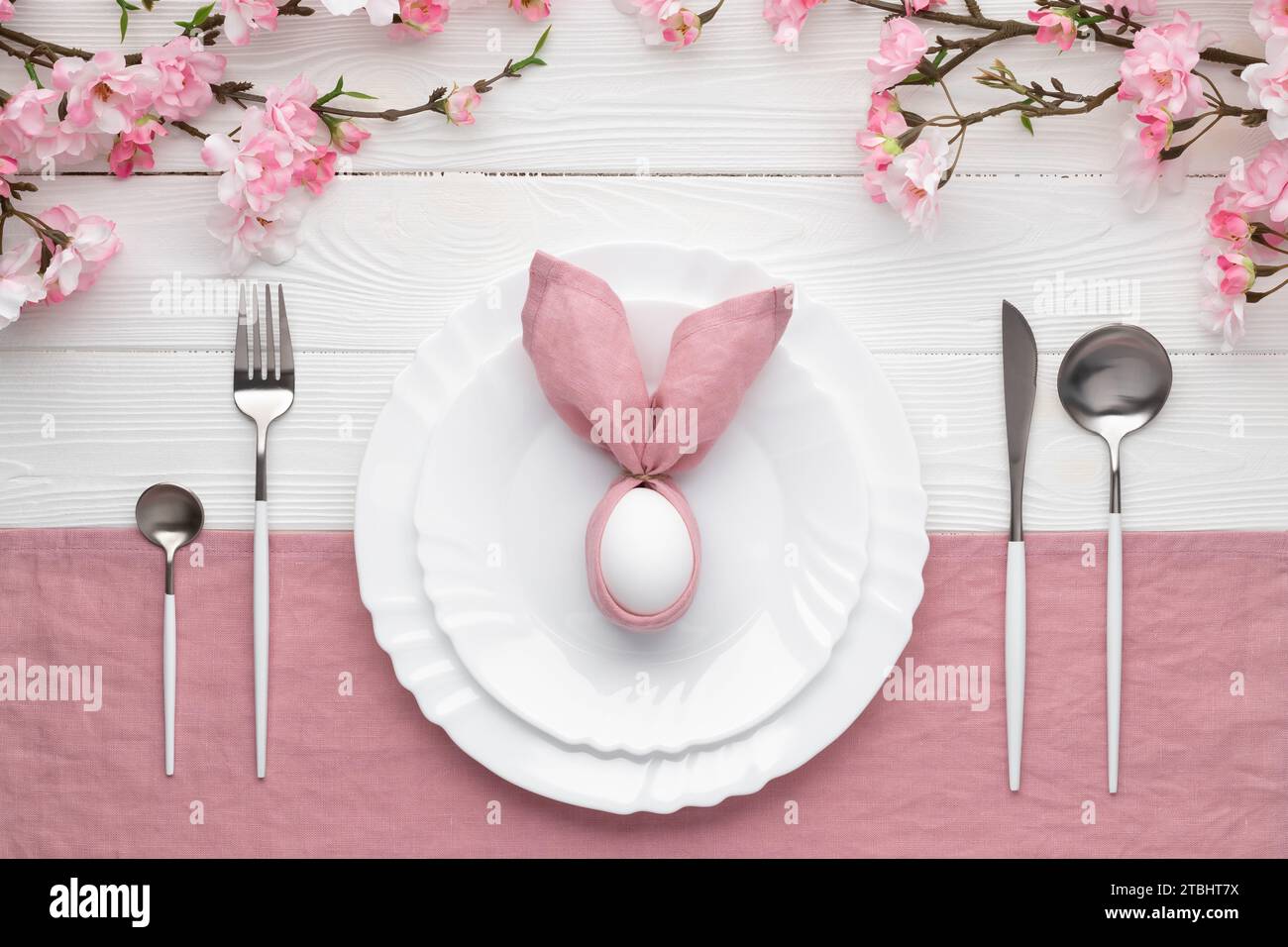 Invitation au déjeuner ou brunch de Pâques. Table de fête avec fleurs printanières roses, couverts. Lapin fait de serviette en lin et oeuf. Joyeuses vacances de Pâques c Banque D'Images