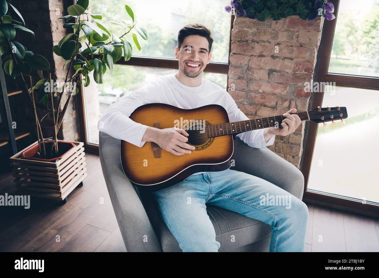 Photo de positif funky jeune gars habillé chemise blanche jouant de l'instrument acoustique à l'intérieur de la salle de la maison Banque D'Images