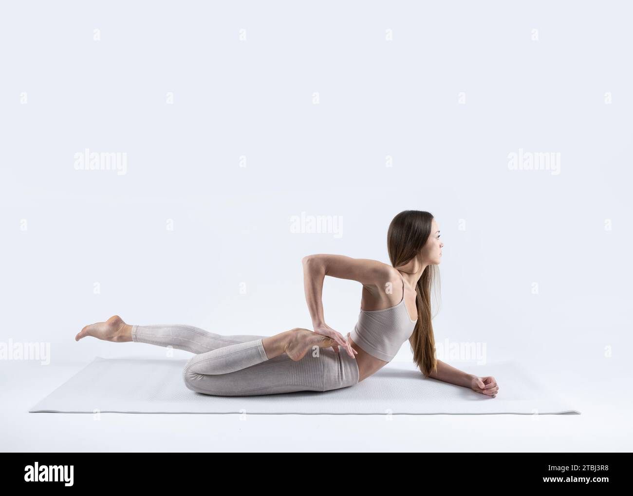 belle jeune femme sportive faisant arda bhekasana (demi-grenouille pose) sur un tapis blanc avec un fond blanc Banque D'Images