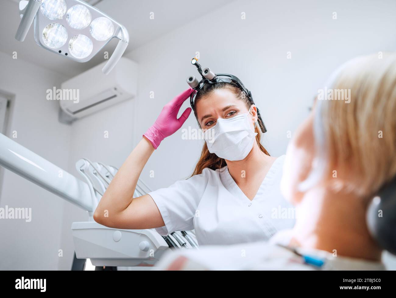 Rendez-vous en clinique dentaire dans un service médical moderne. Dentiste médecin en loupes souriant avec les yeux jeune femme prête pour la chirurgie des dents. Banque D'Images