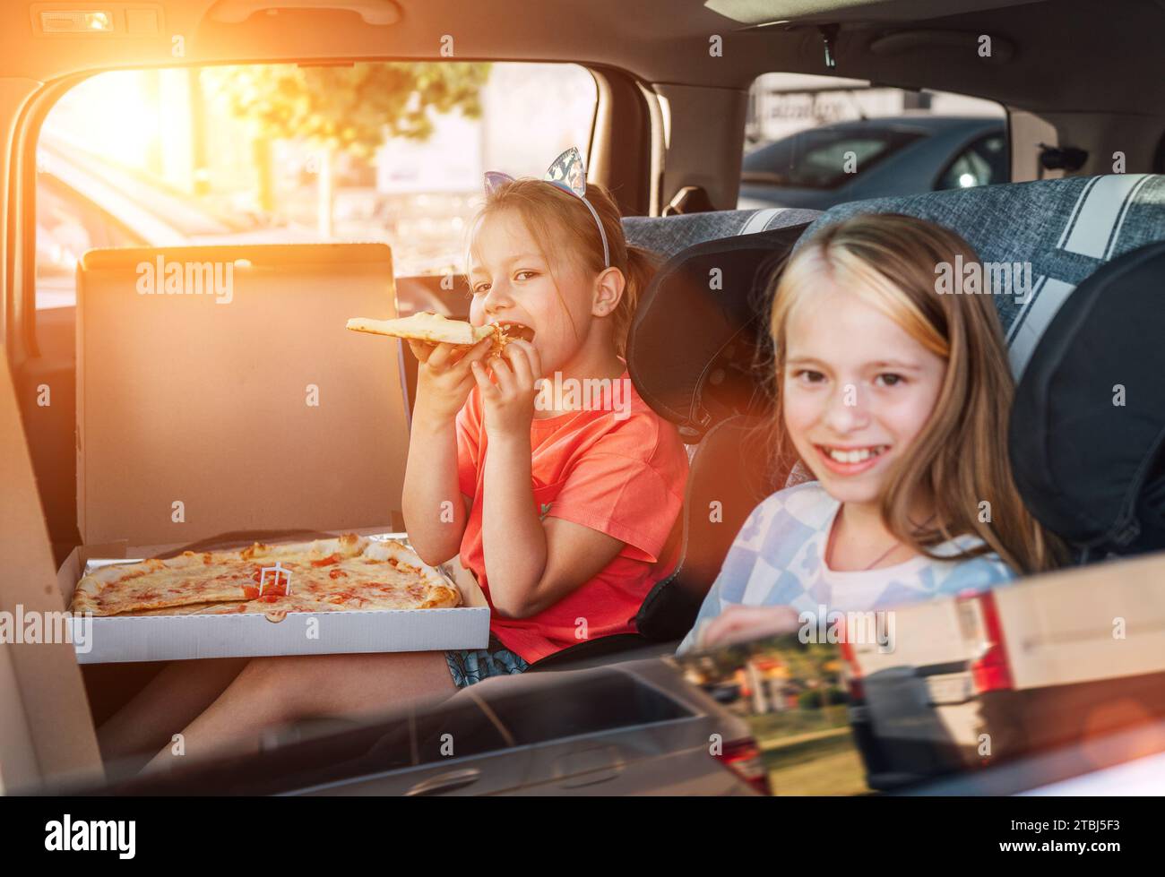 Deux sœurs souriantes et positives sont heureuses de manger une pizza italienne juste cuite dans les sièges d'enfant sur le siège arrière de la voiture. Bonne enfance, restauration rapide ea Banque D'Images