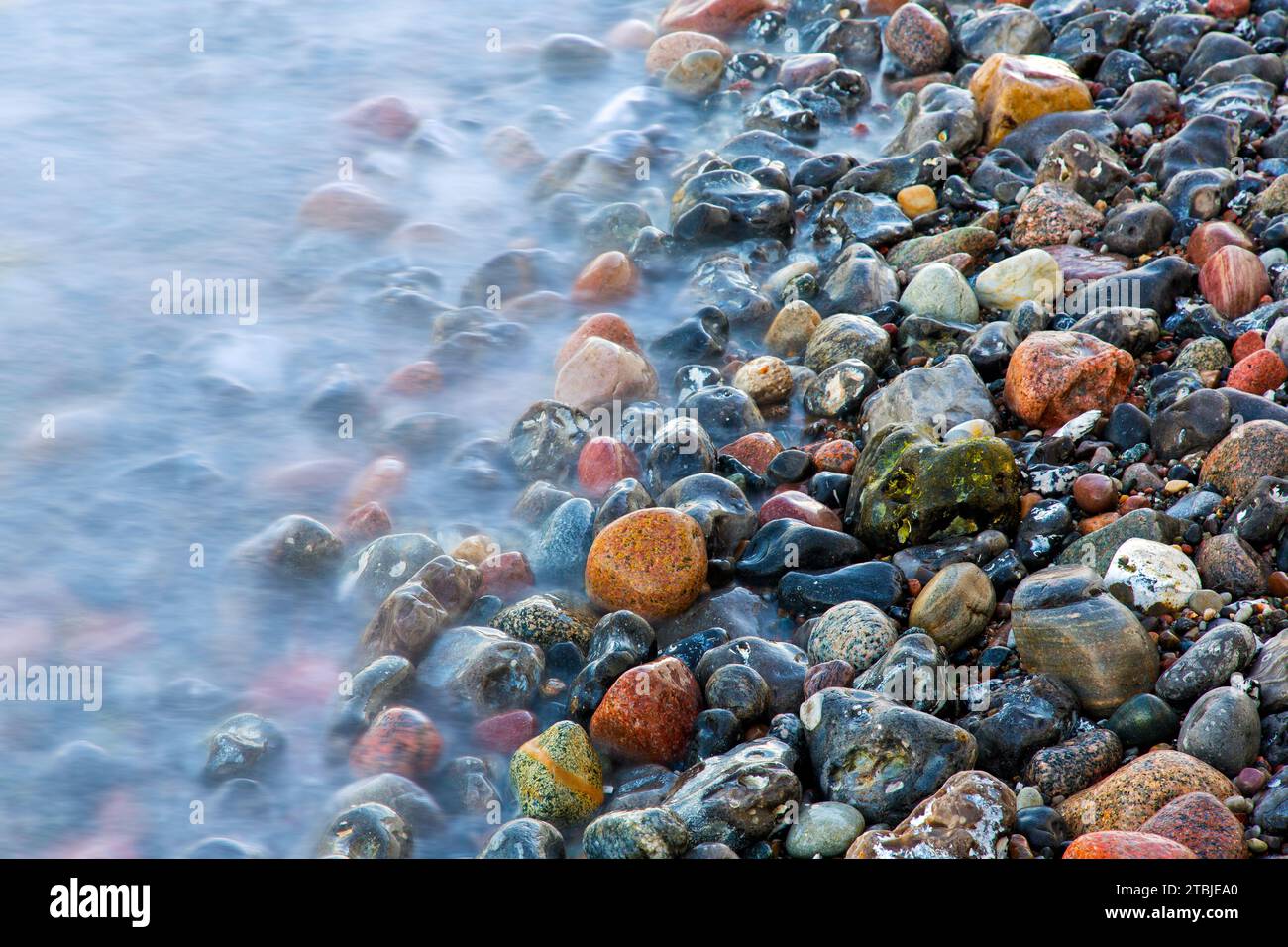 Eau de mer floue de vague roulant sur des galets colorés humides sur la plage de galets / plage de galets Banque D'Images