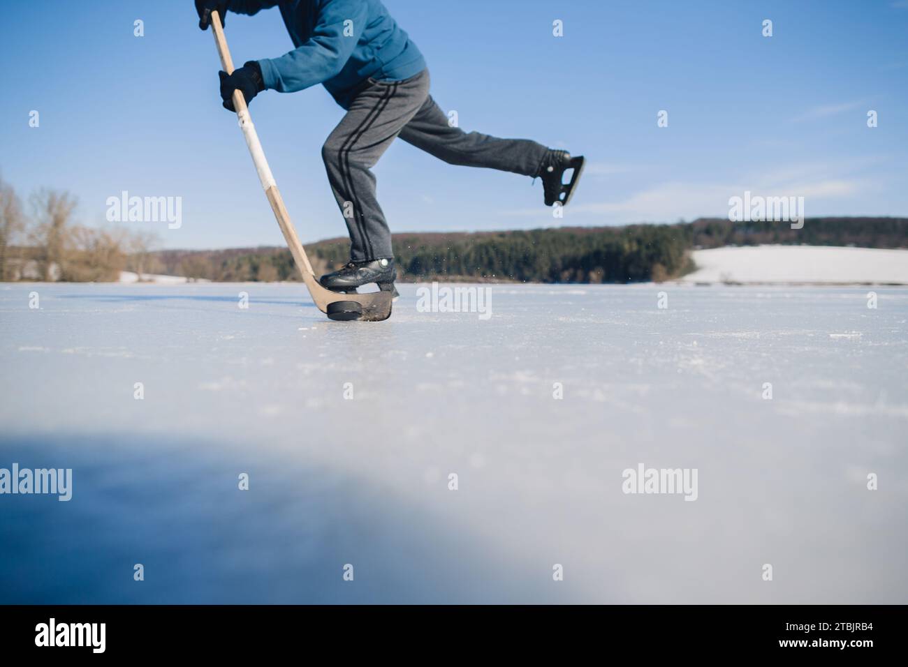 Un homme âgé s'entraîne à frapper la rondelle avec une crosse de hockey sur un lac gelé en hiver. Banque D'Images