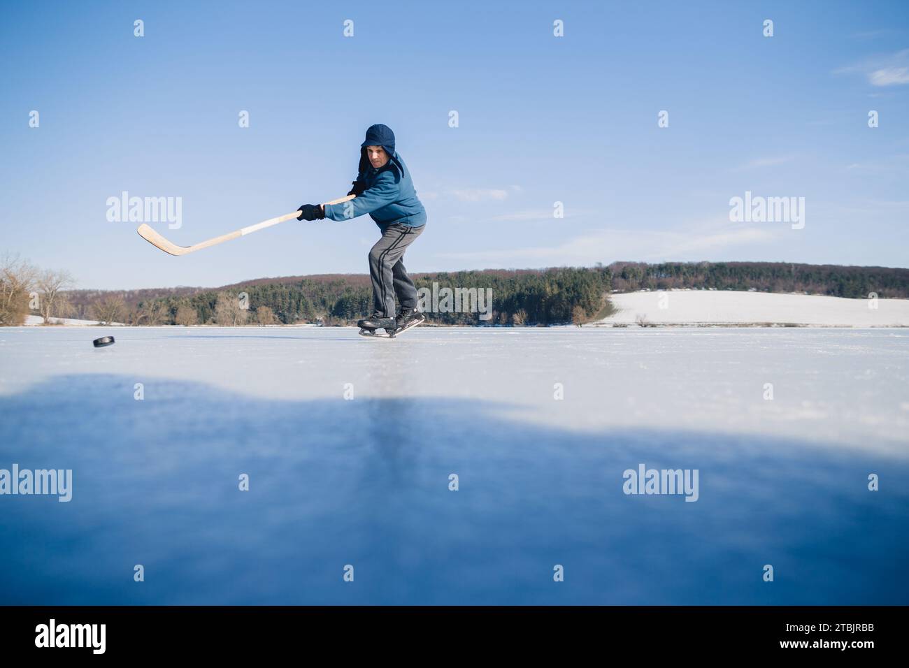 Un homme âgé s'entraîne à frapper la rondelle avec une crosse de hockey sur un lac gelé en hiver. Banque D'Images