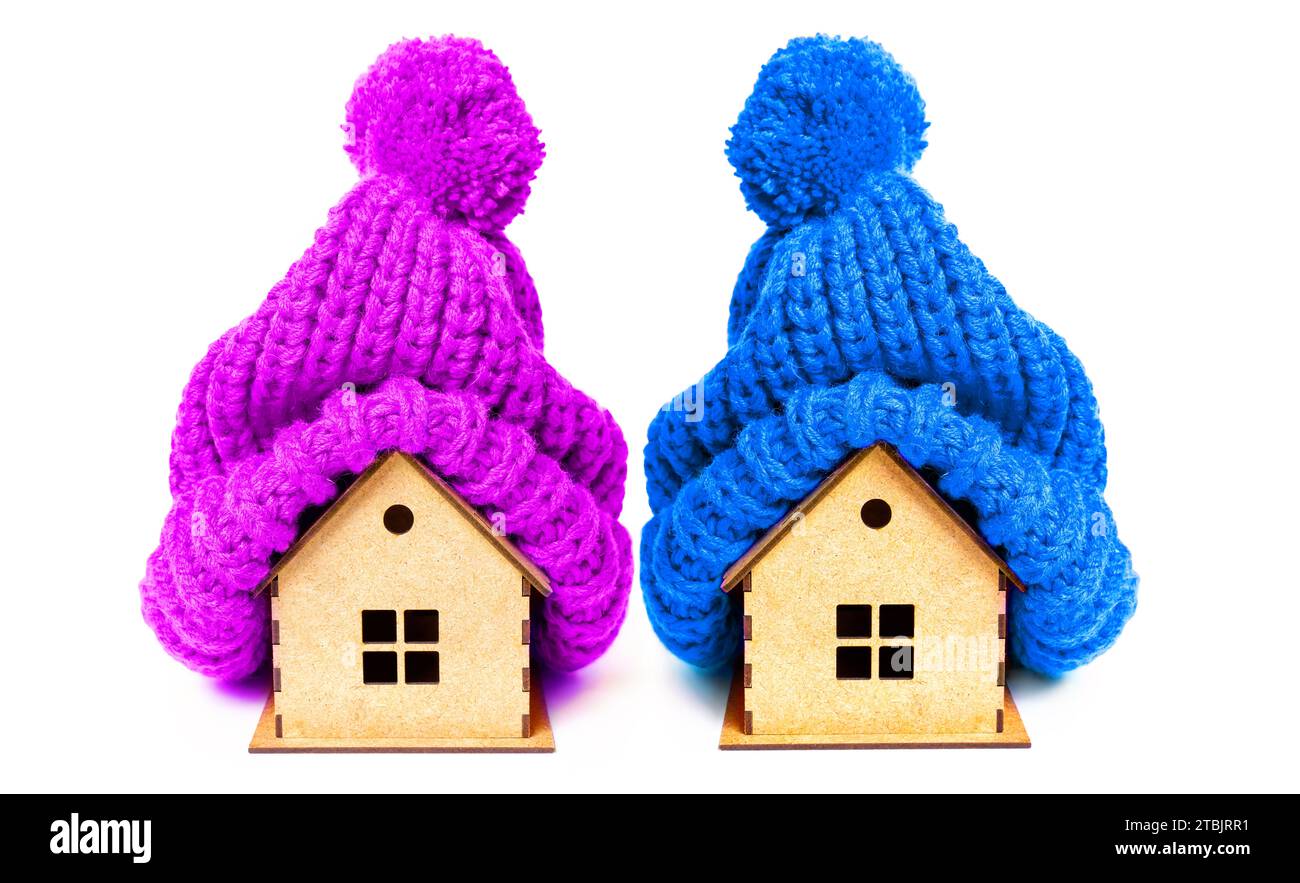 Deux maisons en bois de jouet ornées de chapeaux tricotés douillets avec pompons isolés sur fond blanc. Concept saisonnier, maison et isolation. Banque D'Images