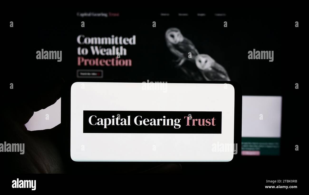 Personne détenant un téléphone portable avec le logo de la société d'investissement britannique Capital Gearing Trust plc (CGT) devant la page Web. Concentrez-vous sur l'affichage du téléphone. Banque D'Images