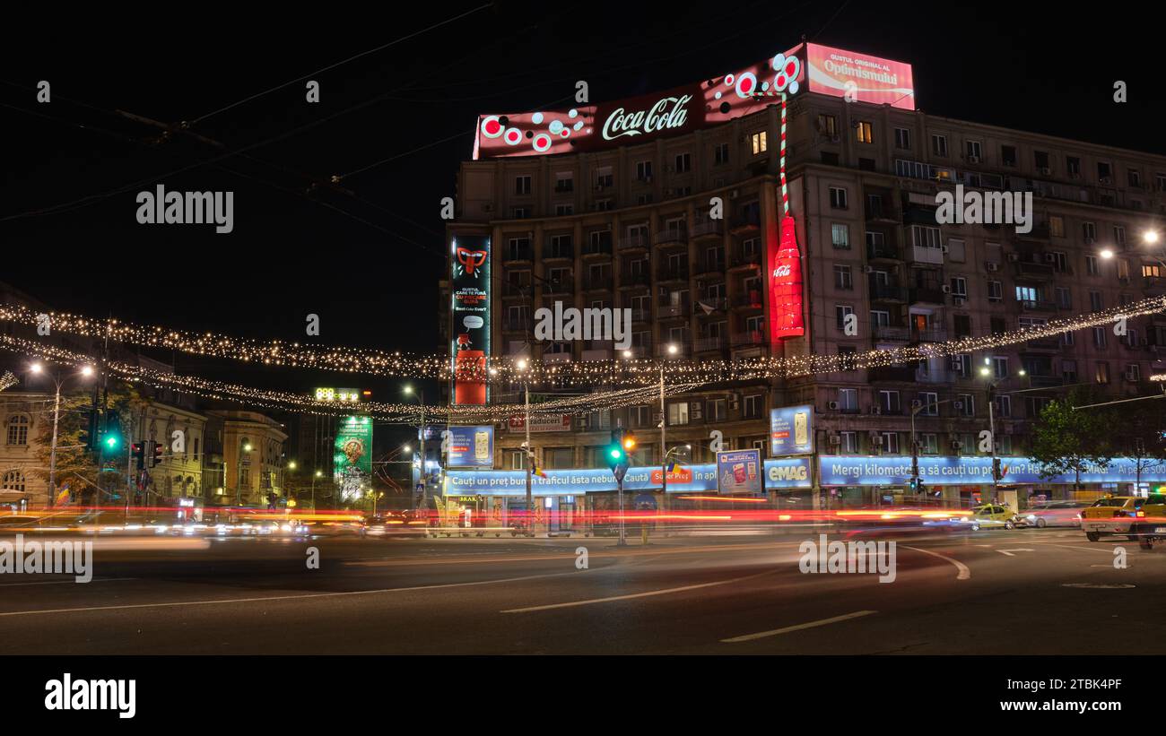 Publicité Coca Cola sur un bâtiment la nuit, avec circulation automobile et lumières festives hivernales sur la place Romana, un monument dans la capitale roumaine. Bucarest, R. Banque D'Images