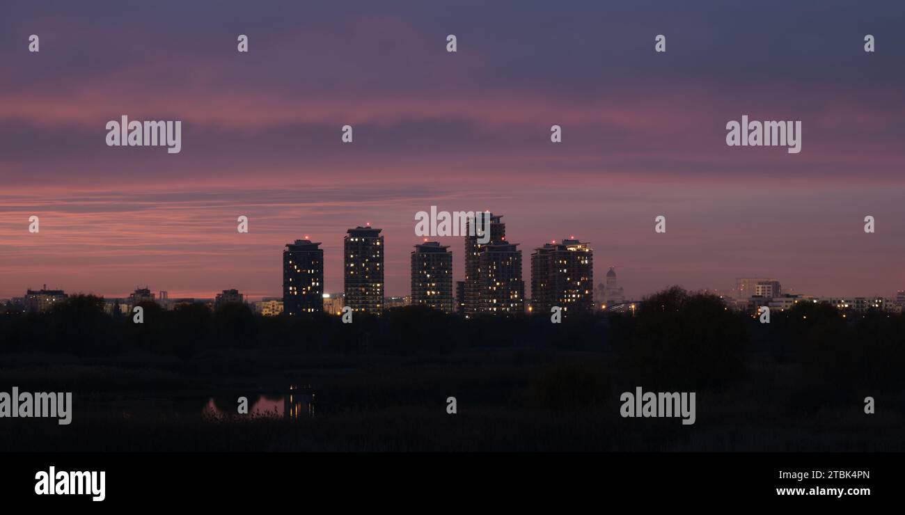 Panorama nocturne de Bucarest dans la capitale roumaine, avec de hauts bâtiments et des couleurs crépusculaires roses et violettes. Banque D'Images