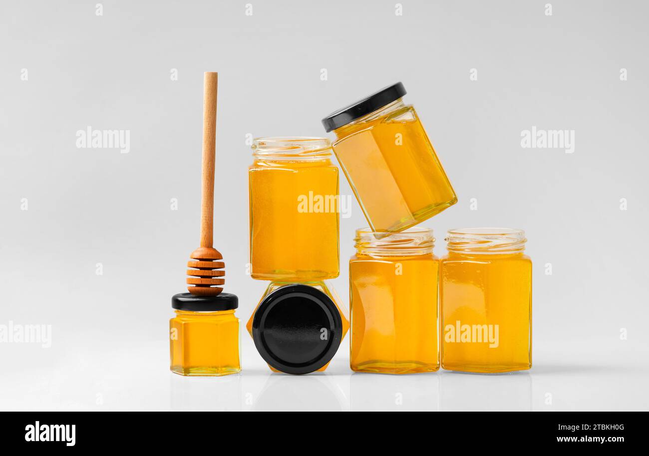 Composition conceptuelle de bocaux en verre sous forme de nids d'abeilles avec du miel et une pelle en bois sur fond blanc. Banque D'Images
