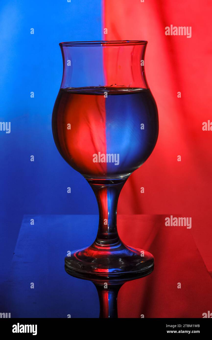 un verre à vin rempli d'eau sur un fond bicolore crée la diffraction et la réflexion de la lumière Banque D'Images