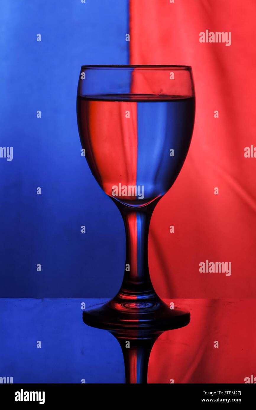un verre à vin rempli d'eau sur un fond bicolore crée la diffraction et la réflexion de la lumière Banque D'Images