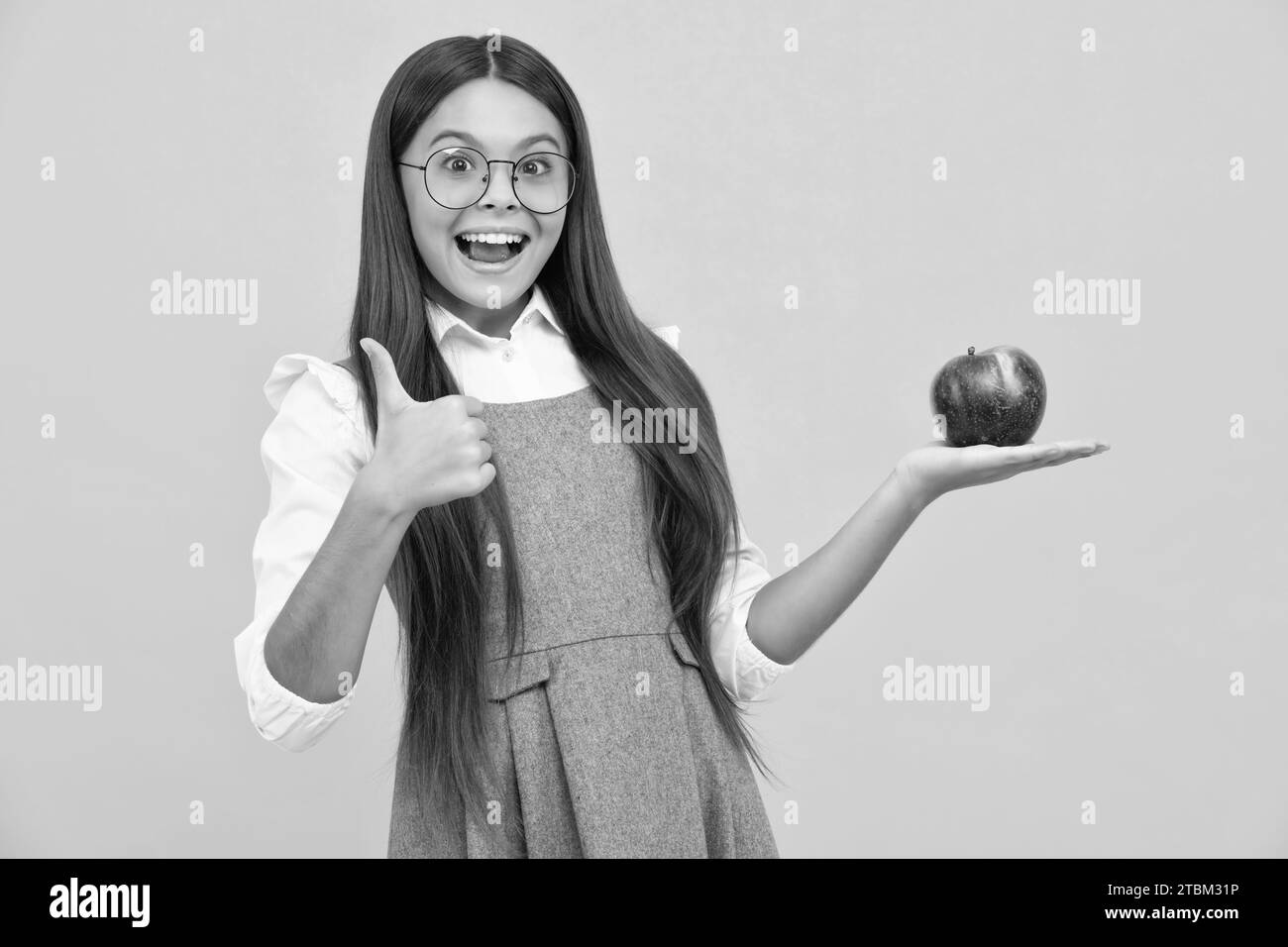 Enfant fille mangeant une pomme sur fond jaune isolé. Tennager avec des fruits. Visage de fille heureux, émotions positives et souriantes. Banque D'Images