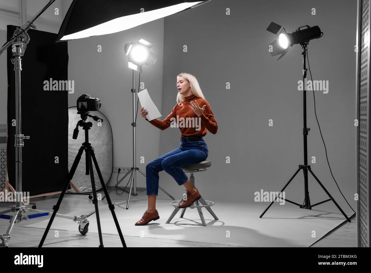 Appel de casting. Femme émotionnelle avec script assis sur la chaise et jouant devant la caméra en studio Banque D'Images