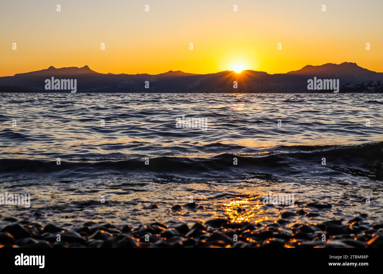 Magnifique coucher de soleil sur la côte méditerranéenne avec les îles et les montagnes. Pierres sur la plage éclairée par la lumière du soleil Banque D'Images