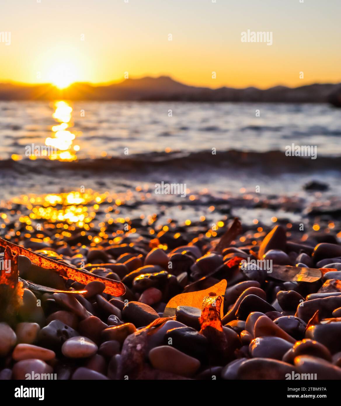 Magnifique coucher de soleil sur la côte méditerranéenne avec les îles et les montagnes. Pierres sur la plage éclairée par la lumière du soleil Banque D'Images