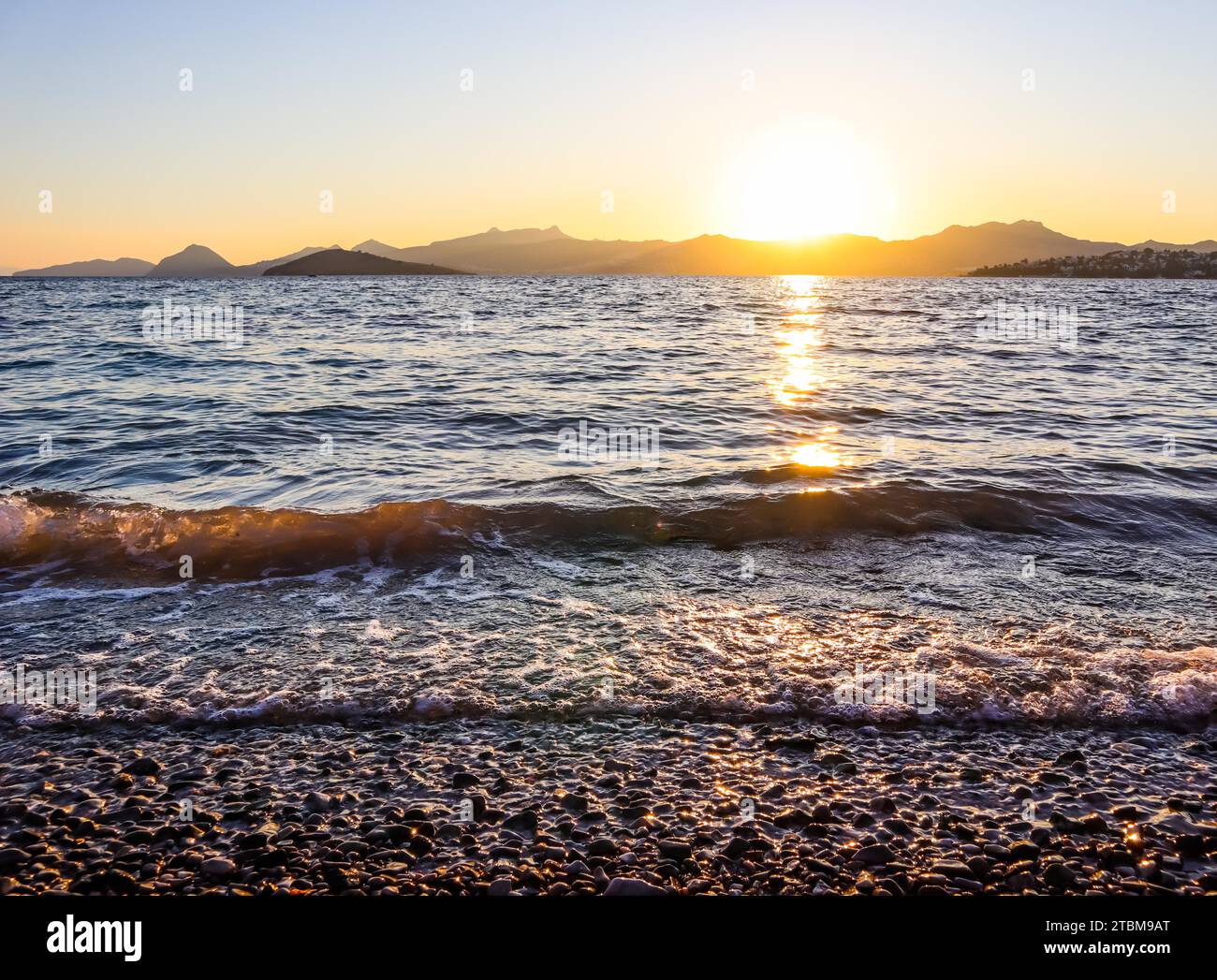 Magnifique coucher de soleil sur la côte méditerranéenne avec les îles et les montagnes. Pierres sur la plage éclairée par la lumière du soleil Banque D'Images