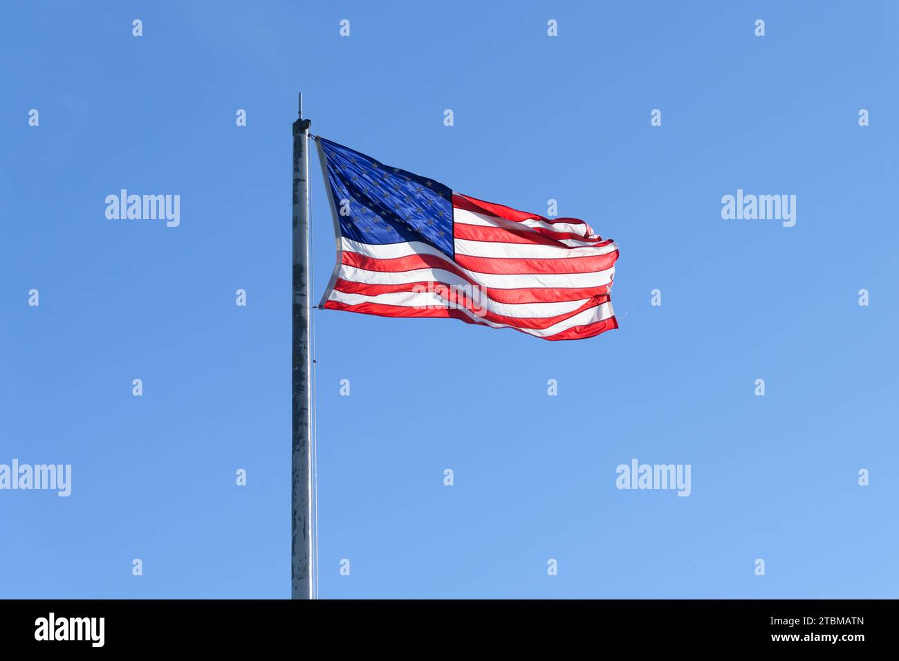 Étoiles et bandes drapeau des États-Unis d'Amérique contre ciel bleu clair avec elle soufflé par le vent Banque D'Images