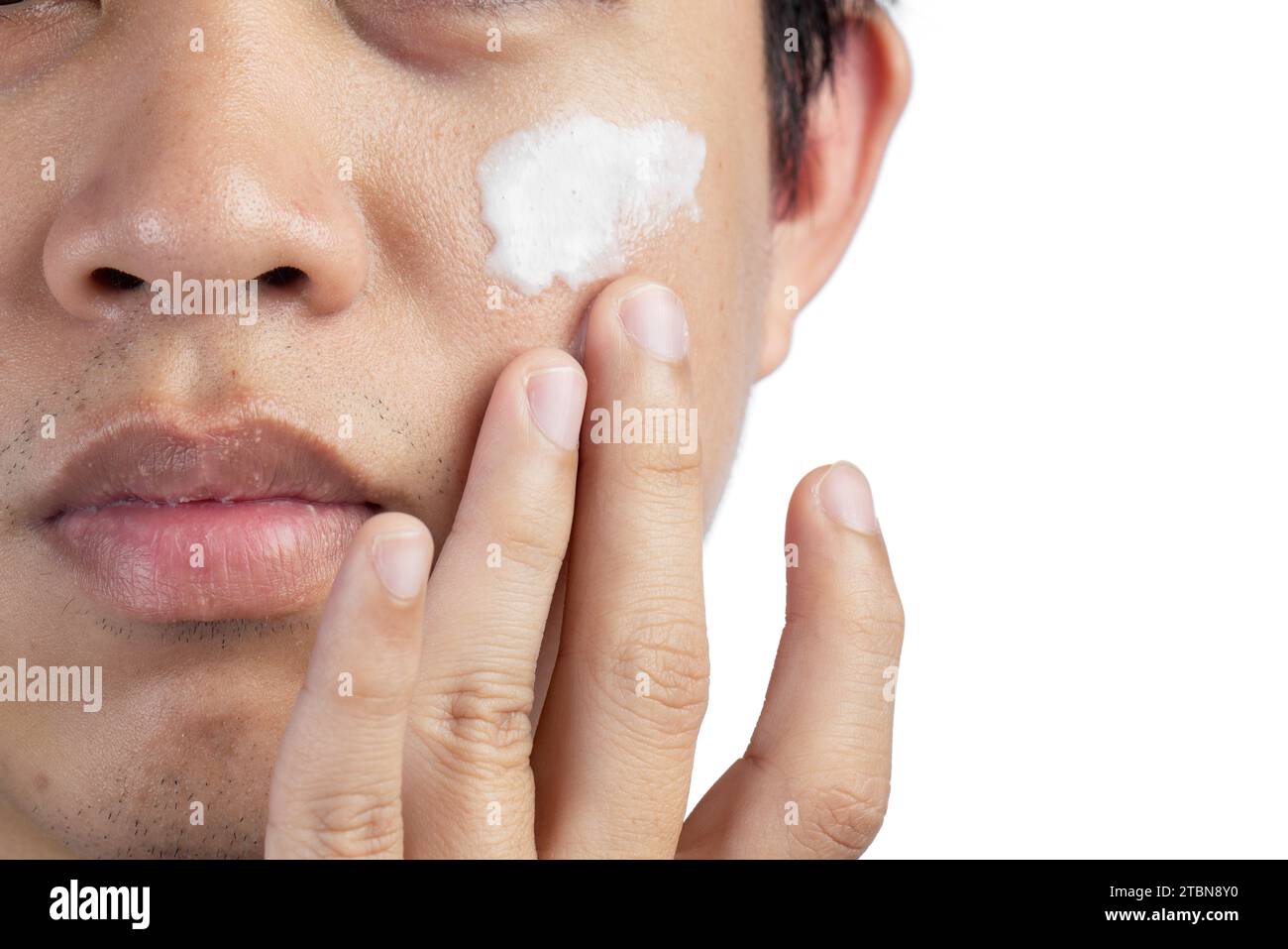 Gros plan portrait de demi-visage jeune homme appliquant de la crème pour le visage isolé sur fond blanc. Banque D'Images
