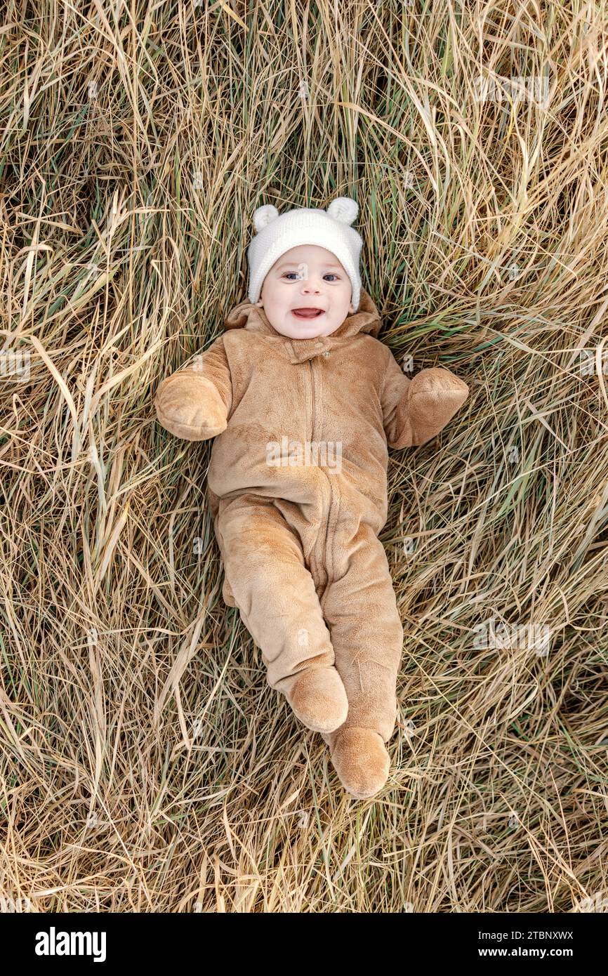 Heureux bébé de 9 mois portant un ours costume couché dans l'herbe d'automne Banque D'Images