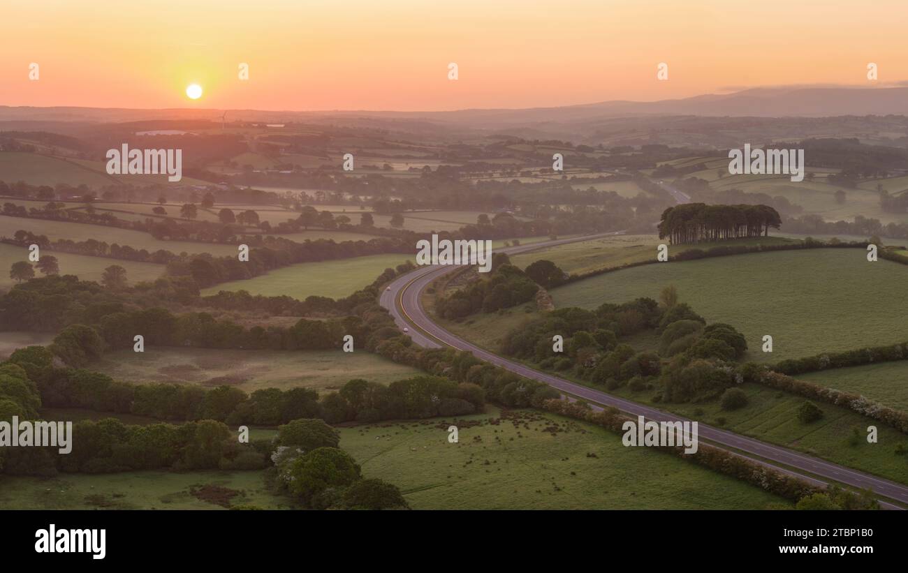Lever du soleil sur l'A30 et Cookworthy Knapp, également connu sous le nom de Nearly Home Trees, Lifton, Devon, Angleterre. Printemps (mai) 2023. Banque D'Images