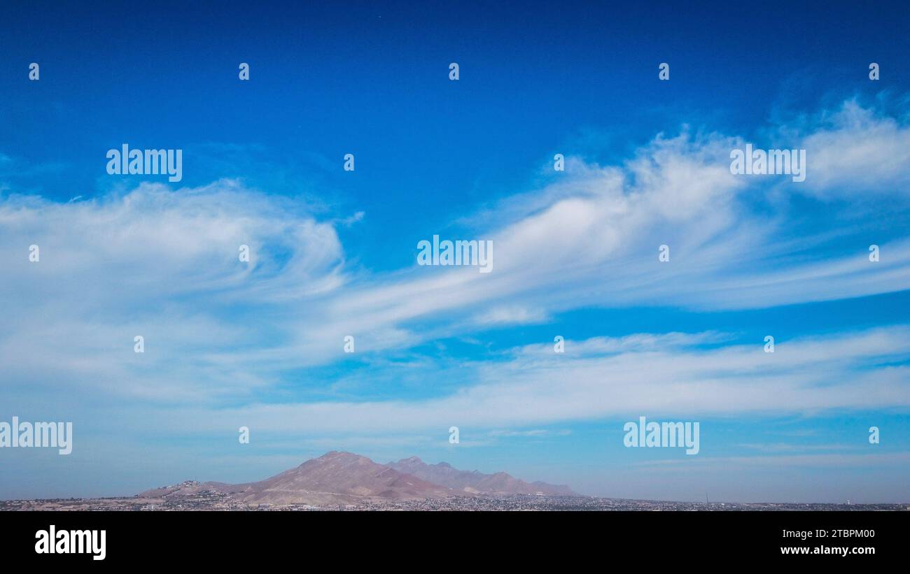 Vue aérienne d'un paysage urbain avec une chaîne de montagnes en arrière-plan, contrastée avec le ciel rempli de nuages blancs moelleux Banque D'Images