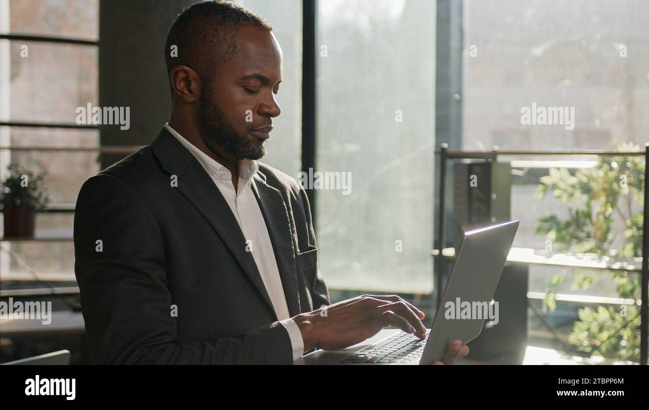Travailleur de bureau adulte mûr ciblé homme afro-américain d'âge moyen des années 40 homme d'affaires ethnique gestionnaire d'employés PDG spécialiste stand avec ordinateur portable tapant sur Banque D'Images