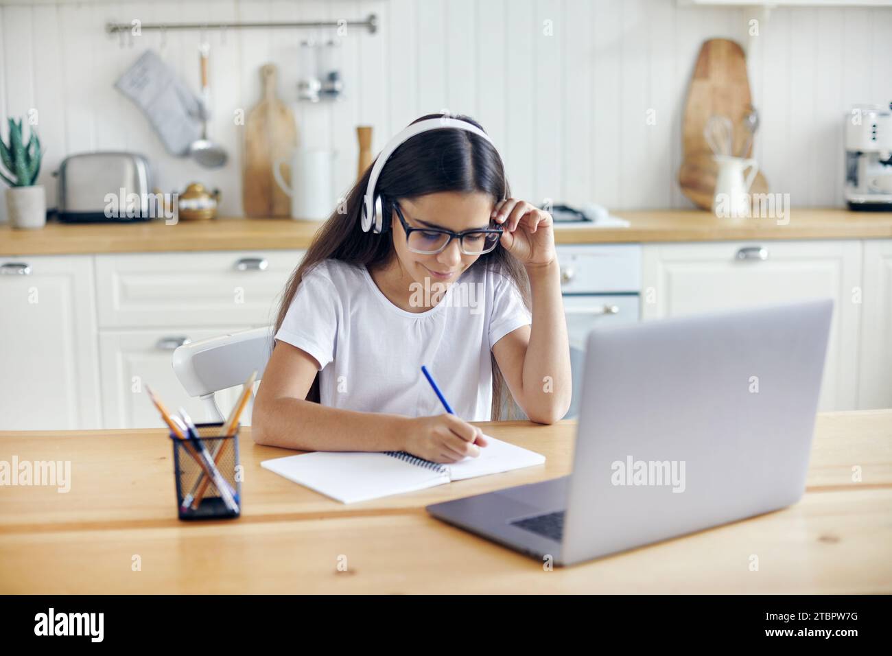 Pré-adolescent 12s fille dans des écouteurs et des lunettes assis à la table e-learns, écouter le cours en ligne, leçon audio, acquérir de nouvelles connaissances, des compétences en utilisant Internet et Banque D'Images
