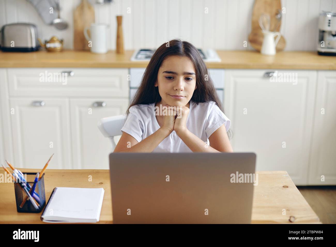 Jolie fille pré-adolescente des années 12 assis à table dans la cuisine regardant le programme éducatif en ligne, nouveau videovlog ou film passer du temps sur Internet seul à la maison. Yo Banque D'Images