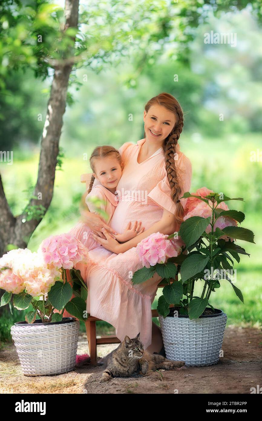 maman souriante heureuse avec une fille enfant sur une journée d'été ensoleillée. Mère et fille enfant dans un beau jardin fleuri avec des fleurs gartensia. Famille heureuse Banque D'Images