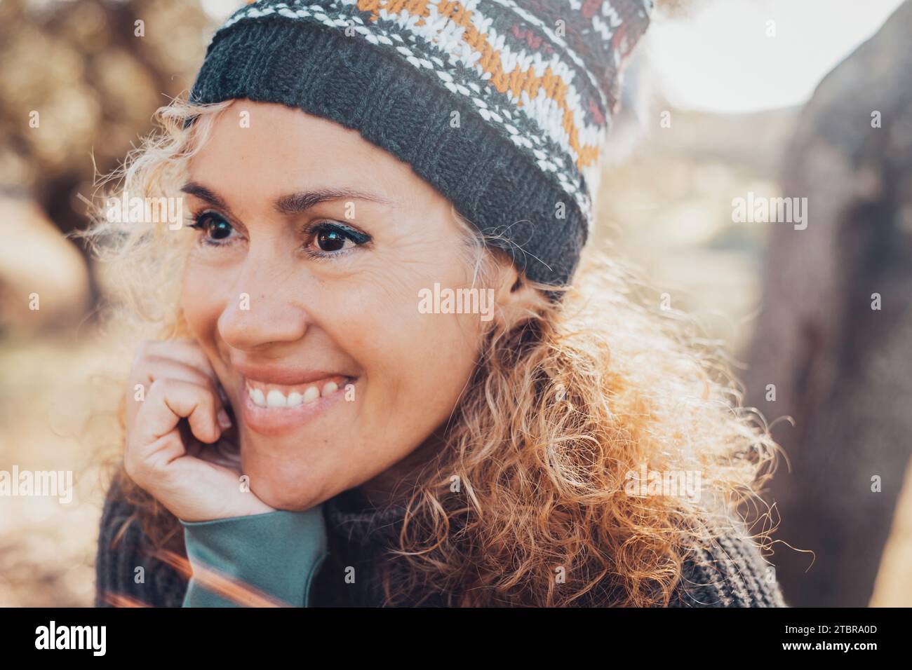 Portrait de mignonne femme heureuse et sereine d'âge moyen souriant et regardant en face d'elle appréciant le temps et les activités de loisirs en plein air au parc pendant la saison d'automne. Porter un bonnet tricoté. Dents parfaites Banque D'Images