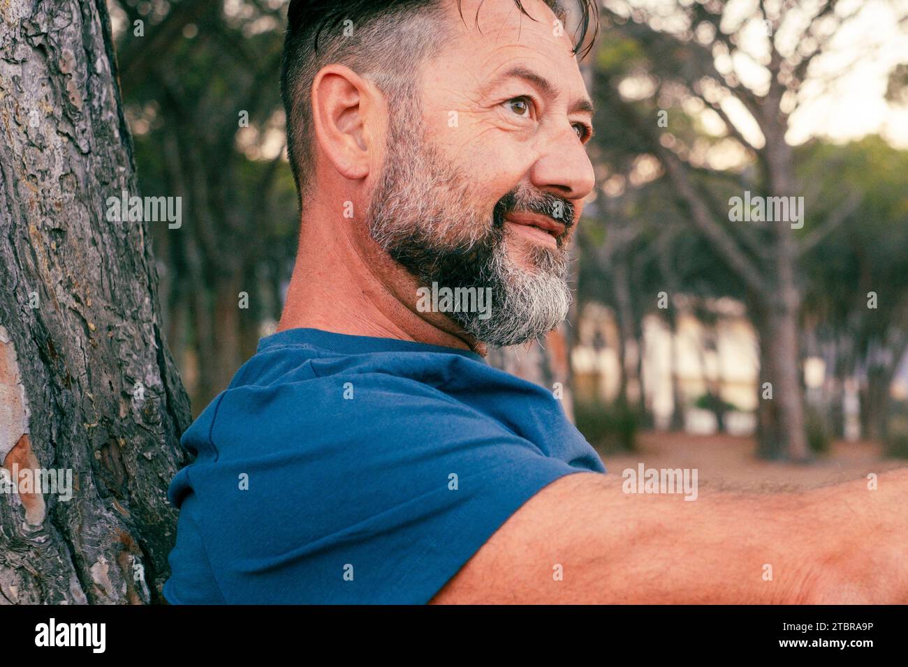 Portrait rapproché latéral d'un homme adulte avec barbe souriant et profitant du temps de détente au parc. Des gens heureux et sereins avec une expression joyeuse. Bonne journée. Beau mâle 50 ans dehors. Lieu de la nature Banque D'Images