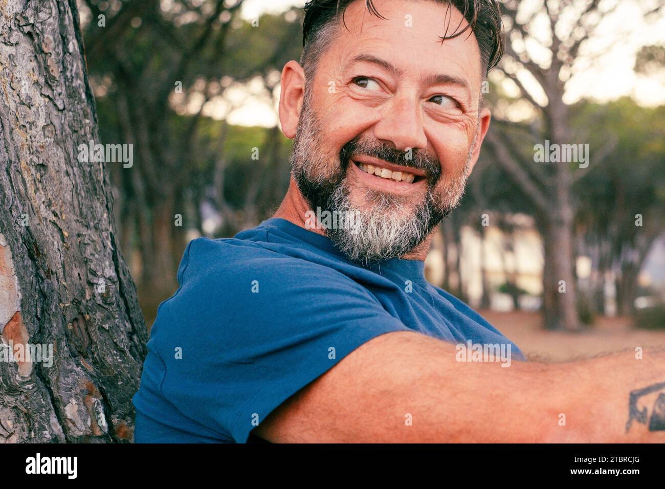 Portrait rapproché latéral d'un homme adulte avec barbe souriant et profitant du temps de détente au parc. Des gens heureux et sereins avec une expression joyeuse. Bonne journée. Beau mâle 50 ans dehors. Lieu de la nature Banque D'Images